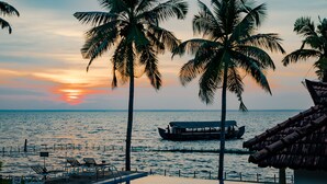 A poolside view with a sunset, palm trees, and a boat on the water. - Backwater Ripples Kumarakom (Kottayam)
