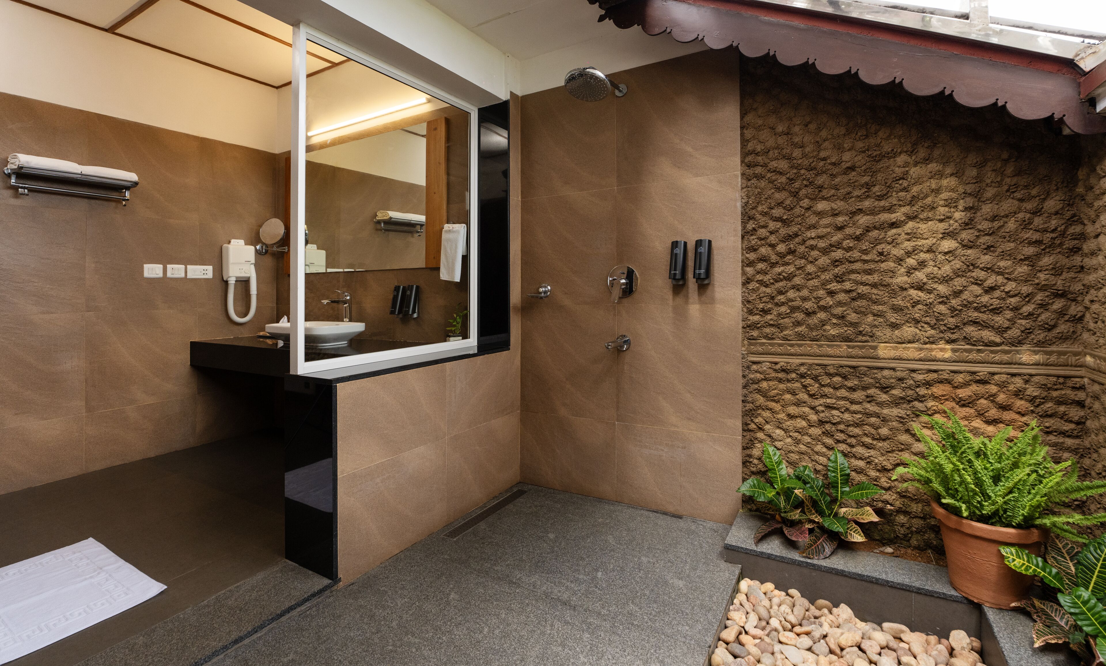 Een moderne badkamer met een grote spiegel, een wastafel en een douche. Buiten staan planten en een kleine rotstuin.