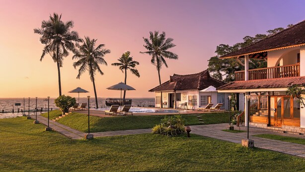 A beachfront property with a pool, lounge chairs, and palm trees. - Backwater Ripples Kumarakom (Kottayam)