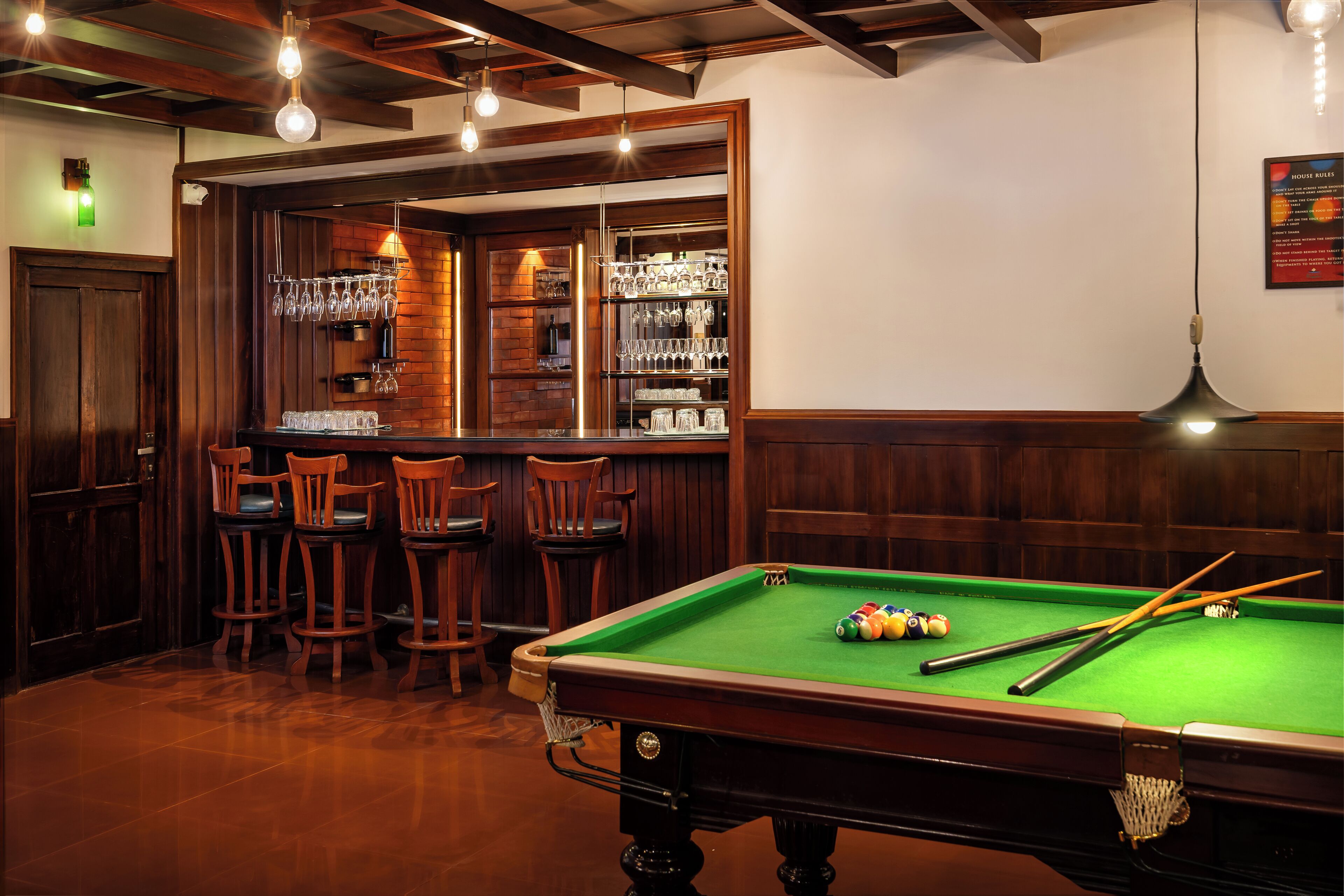 Una mesa de billar con bolas, una zona de bar con taburetes y una pared de ladrillo.