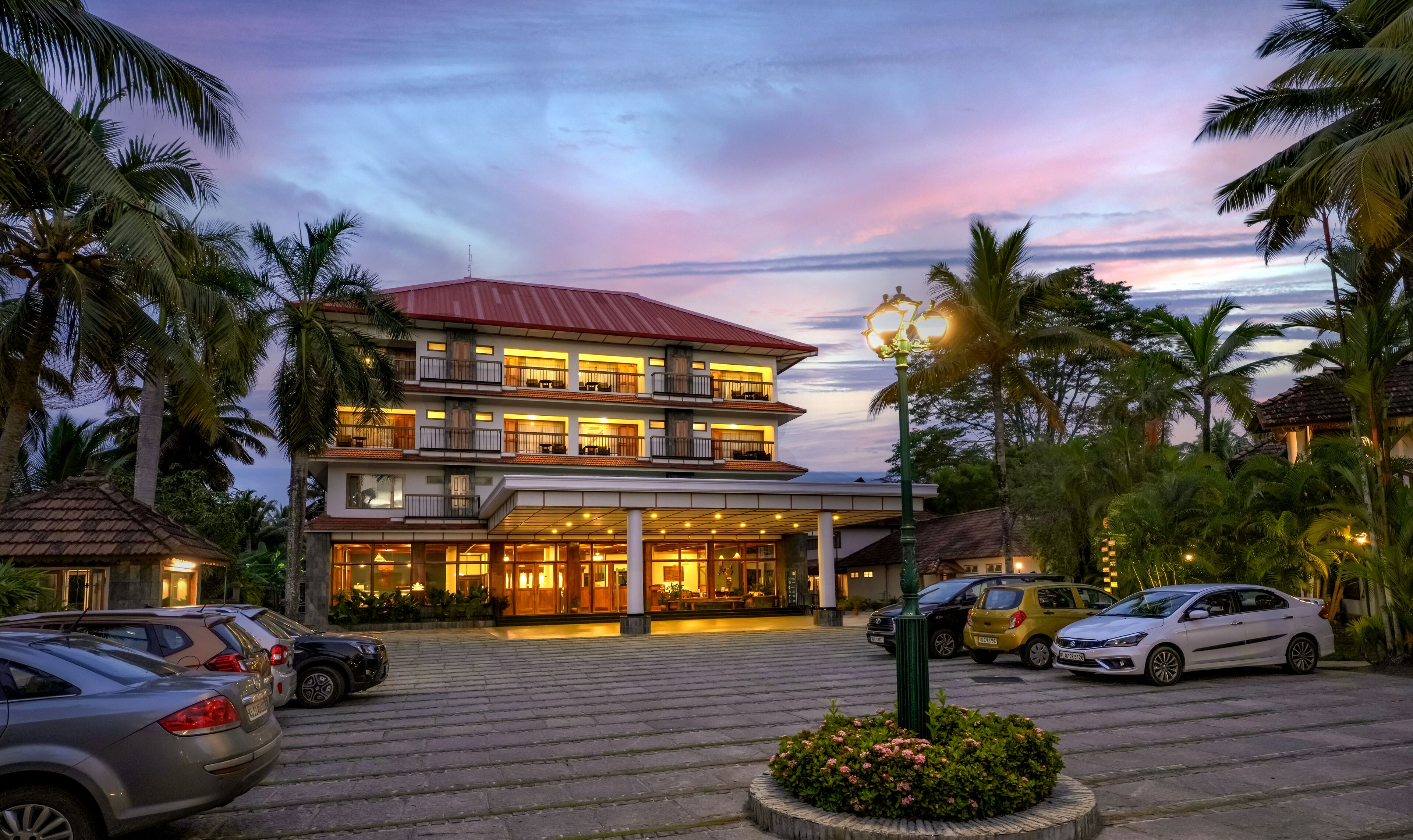 A multi-story hotel with a red roof, multiple balconies, and a well-lit entrance.