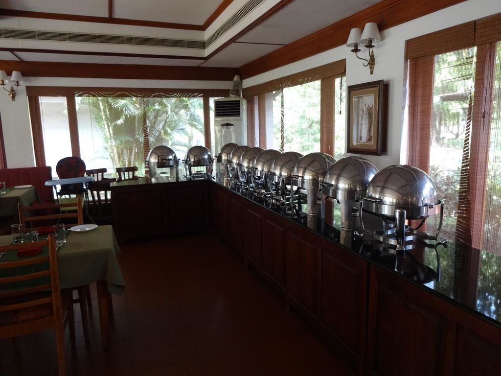 A buffet setup with multiple serving stations, a dining area with tables and chairs, and large windows with blinds.