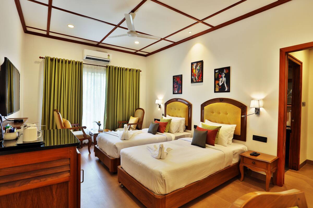 A hotel room with two beds, a desk, a chair, a TV, and artwork on the walls.