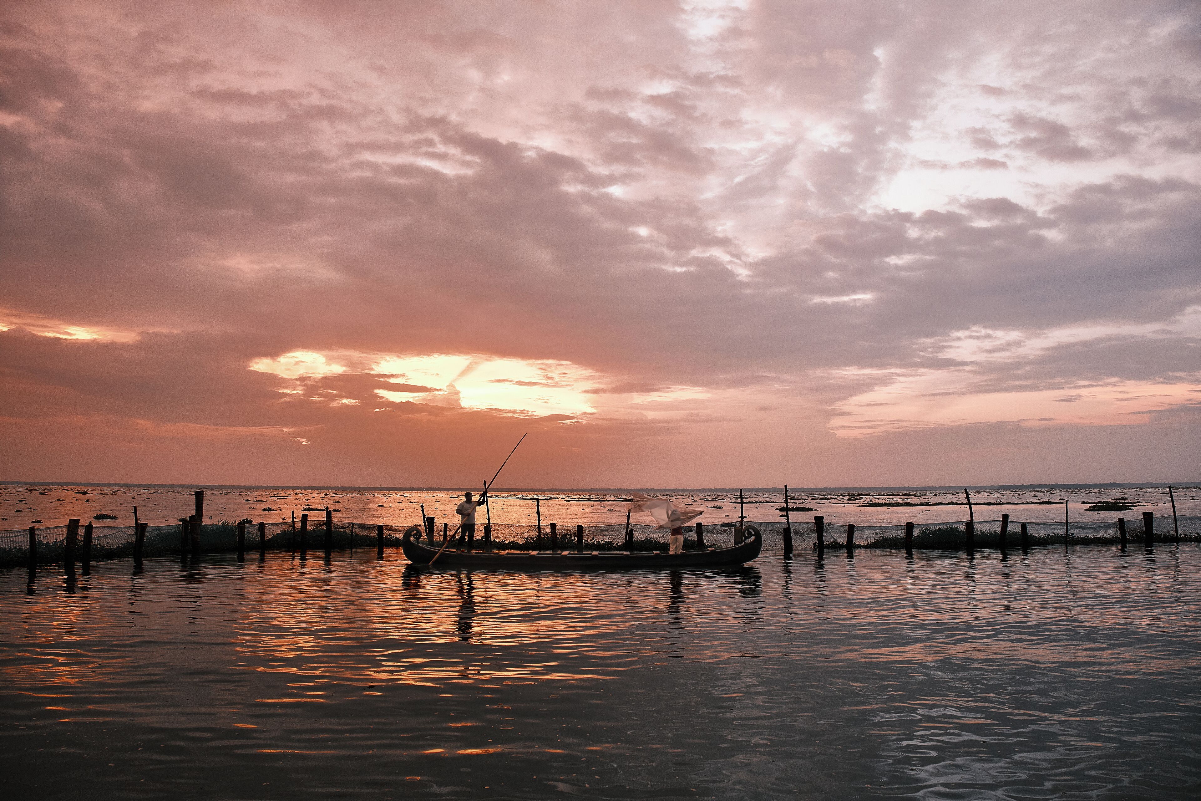 Um pôr do sol sobre águas calmas, com um barco e uma pessoa em seu interior.