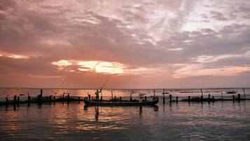 Um pôr do sol sobre águas calmas, com um barco e uma pessoa em seu interior.