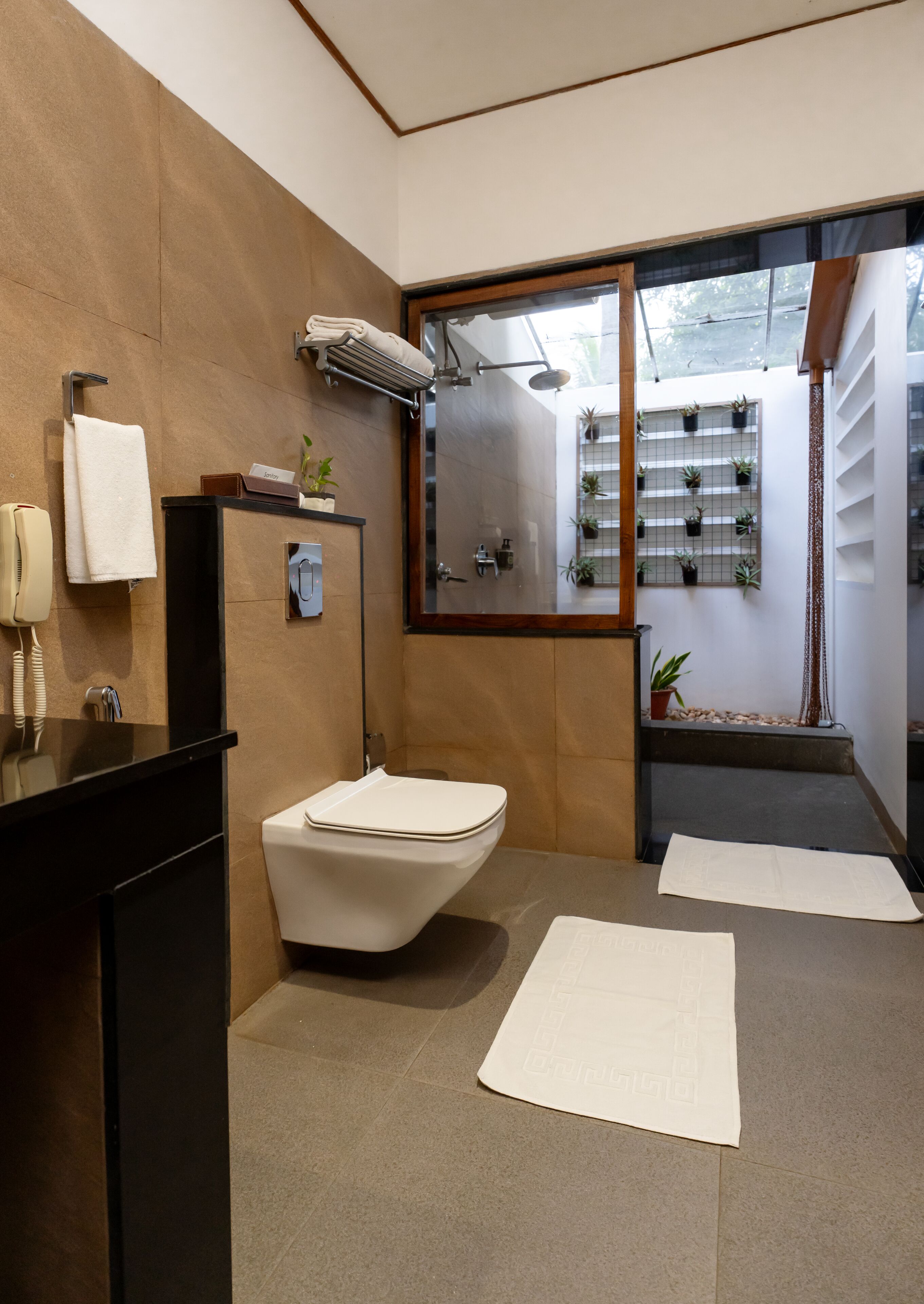 A modern bathroom with a toilet, sink, and shower. There is a mirror above the sink and a window with plants on the windowsill.