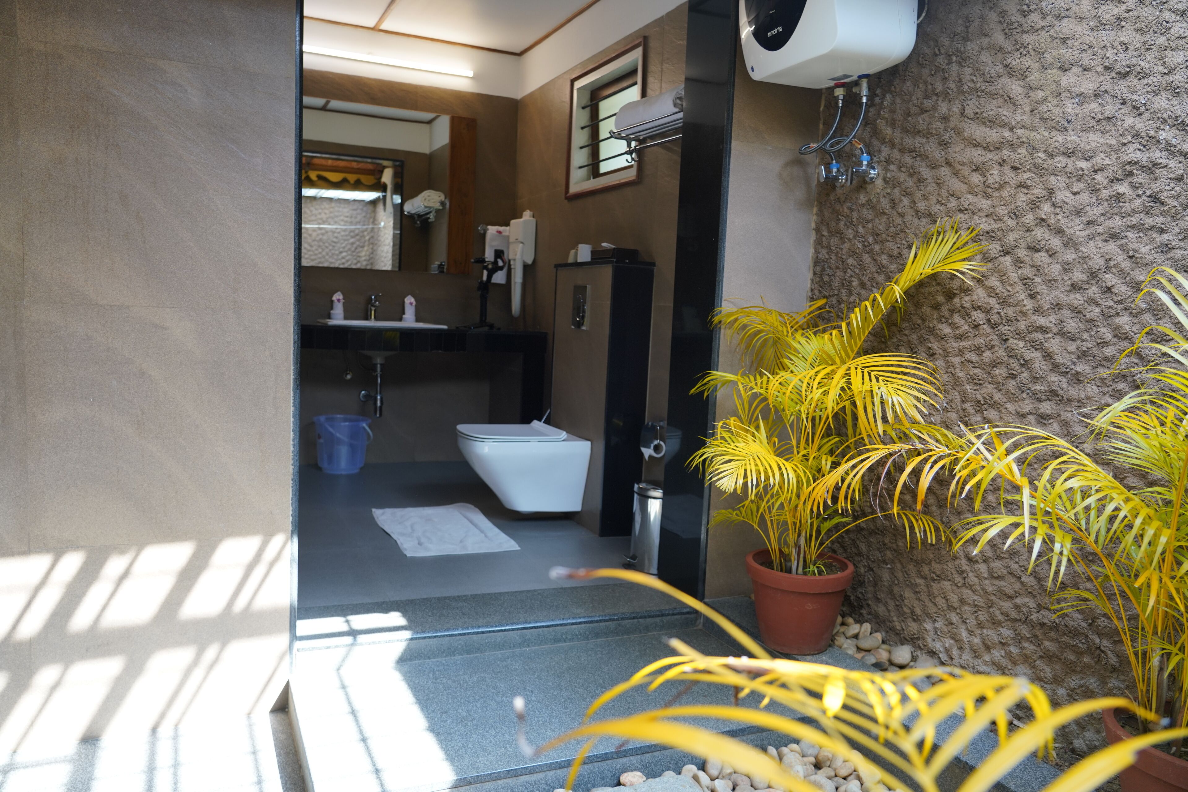 A modern bathroom with a toilet, sink, and mirror. There are potted plants and a towel rack.