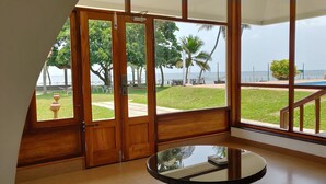 A room with large glass doors leading to a balcony with a view of the sea and palm trees. - Backwater Ripples Kumarakom (Kottayam)