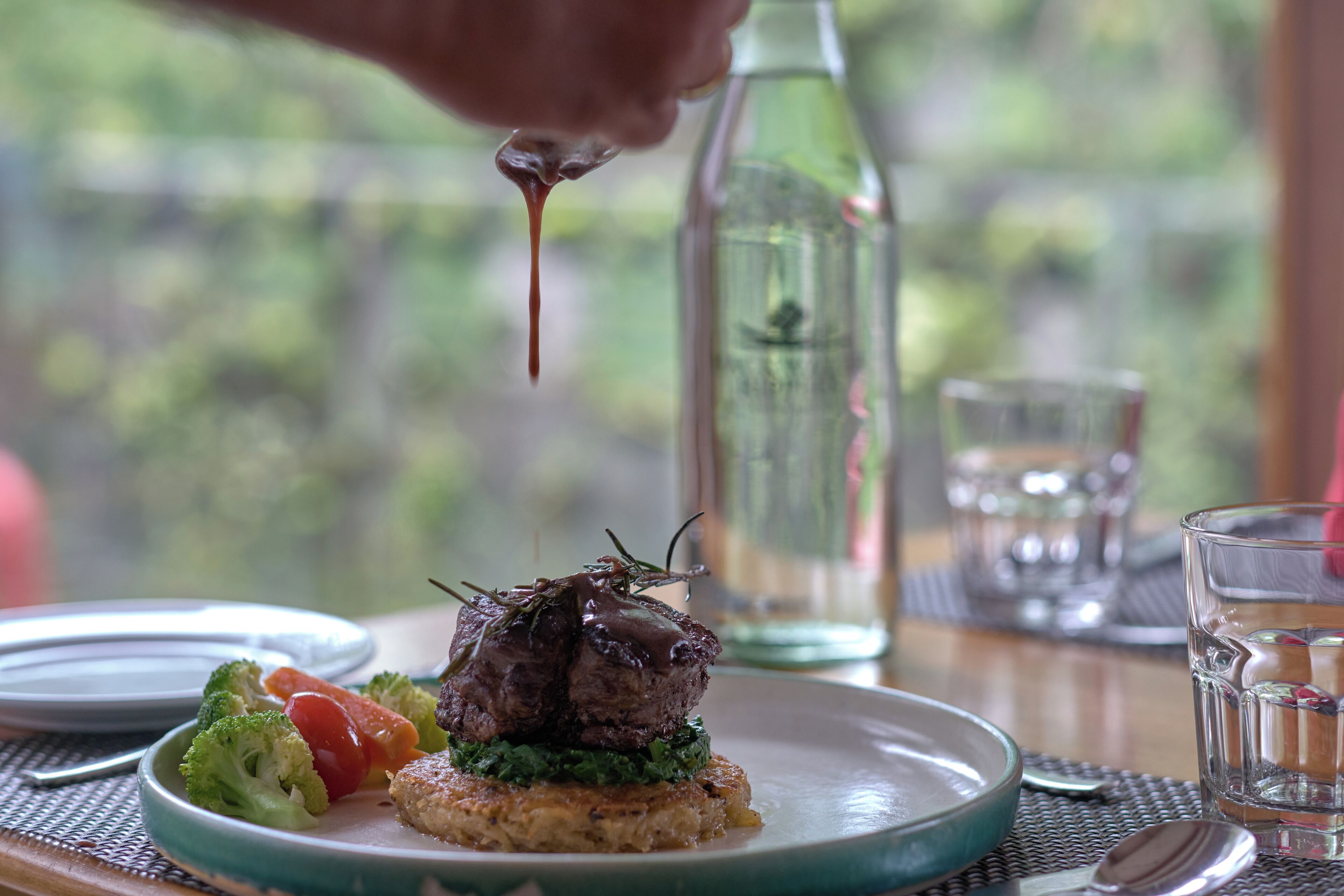 A plate with a steak, vegetables, and sauce being poured on top.