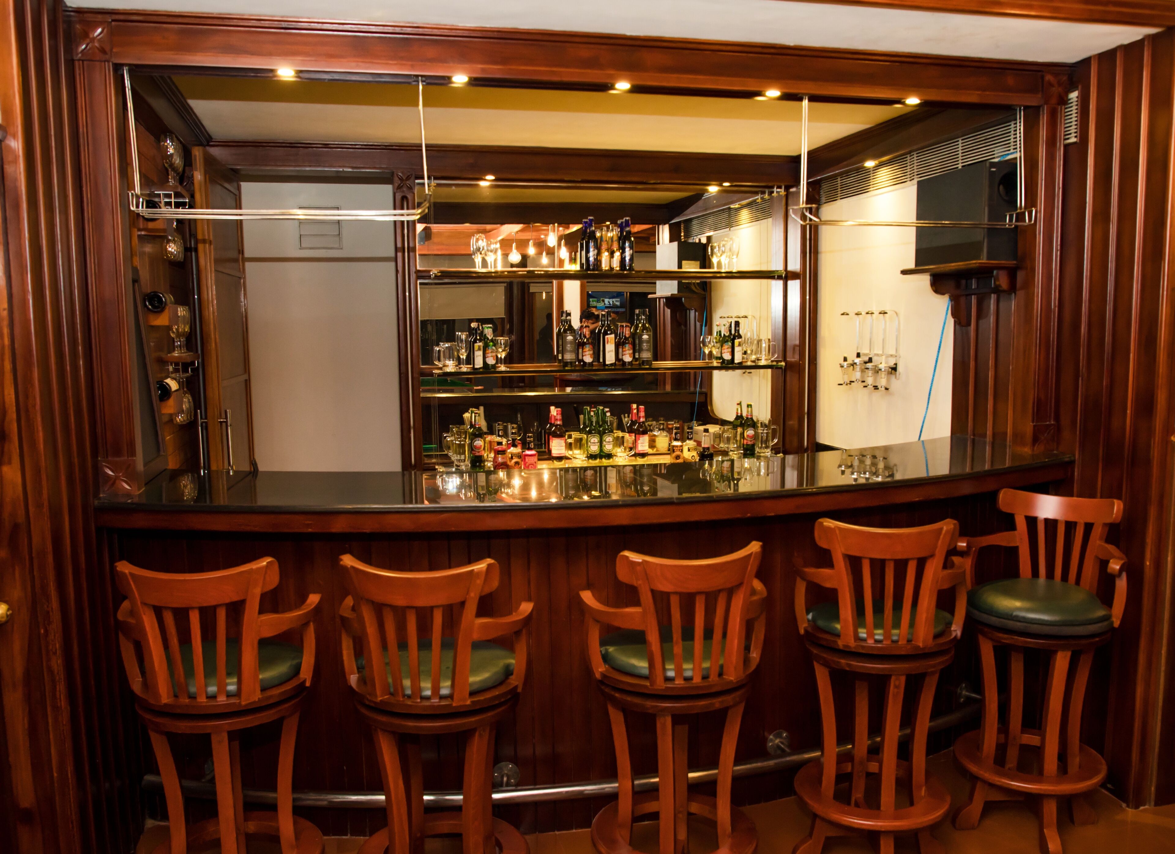 Un espace bar doté d’un long comptoir, de nombreuses chaises et d’un mur miroir qui reflète le bar.