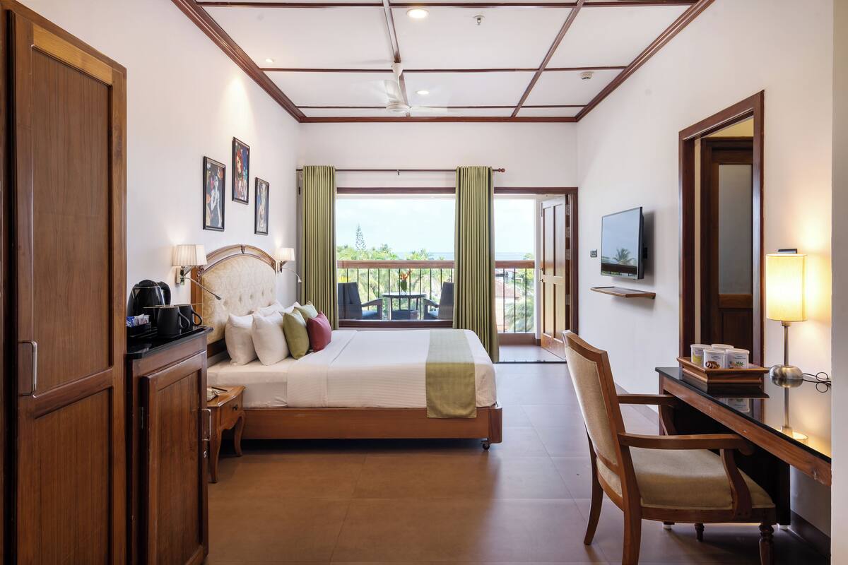 A hotel room with a bed, a desk, a chair, a TV, and a balcony with a view.