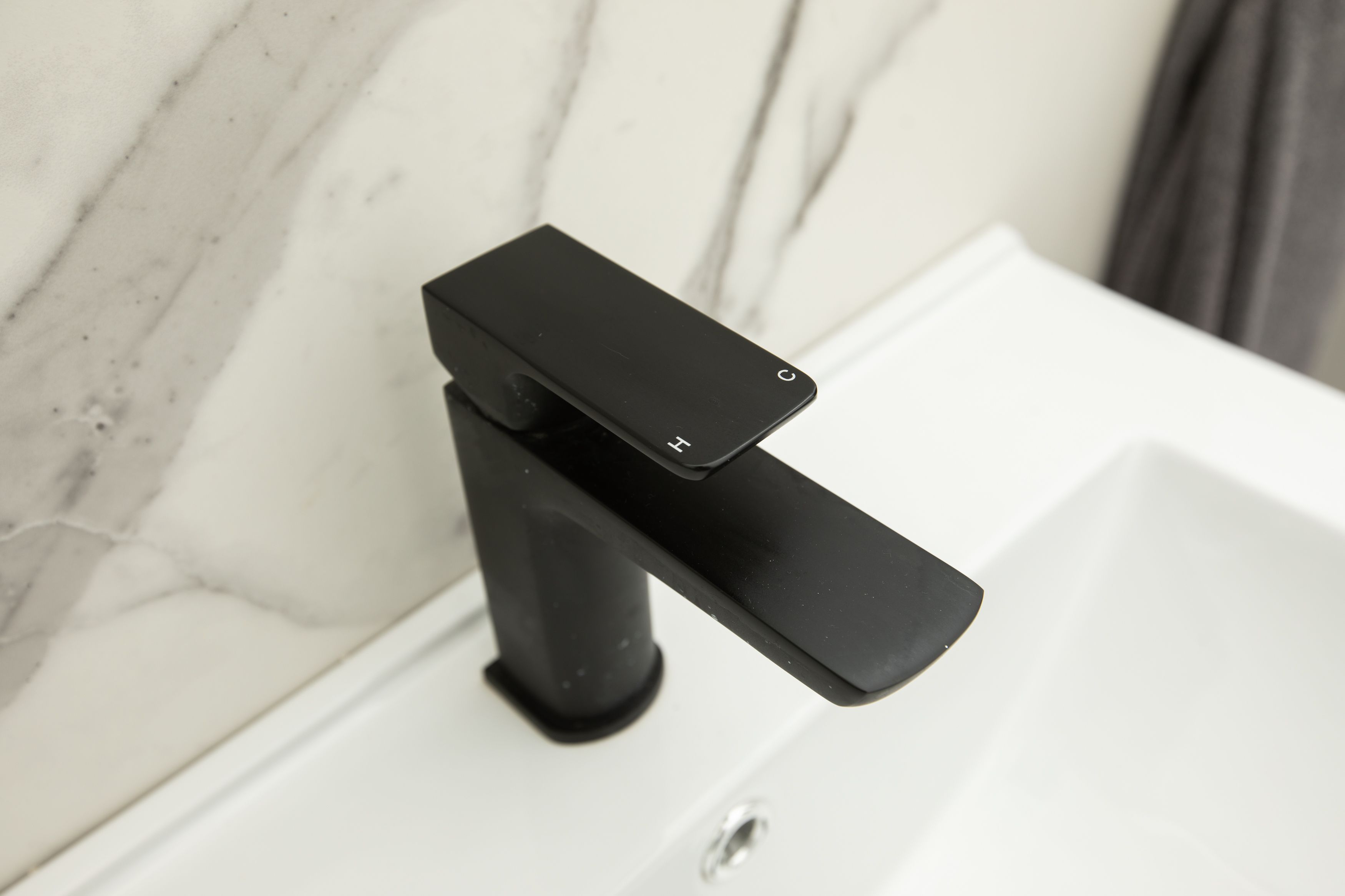 A modern bathroom with a black faucet mounted on a white sink.