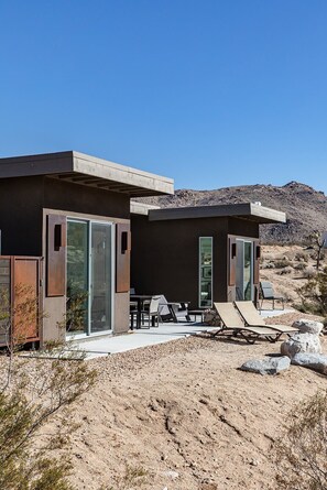 A modern building with a patio area, outdoor seating, and a desert landscape in the background.