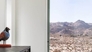A modern room with a large window, a white chair, a dark wooden cabinet, and a decorative bird. - Shelter 2 By Homestead Modern (Joshua Tree)