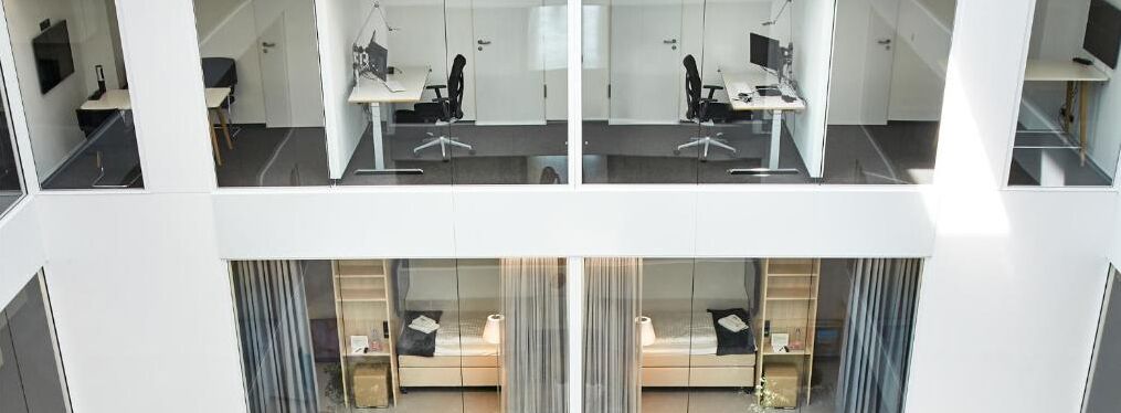 A modern office space with multiple workstations, glass partitions, and a view of the lower level.
