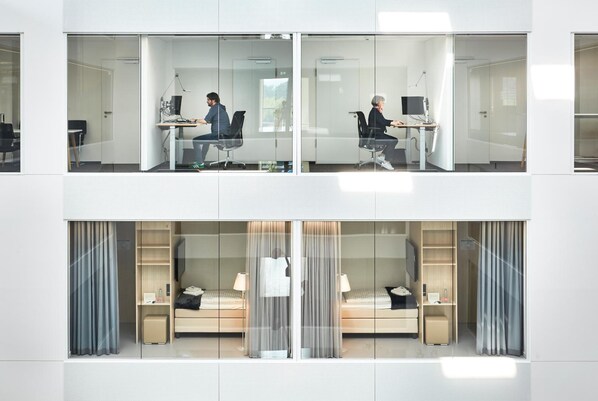 A modern hotel room with a glass partition, a bed, a desk, and a chair. - Hotel Vivendi (Paderborn)