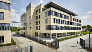 Un edificio moderno de varios pisos, con amplios ventanales, techo plano y un patio empedrado.