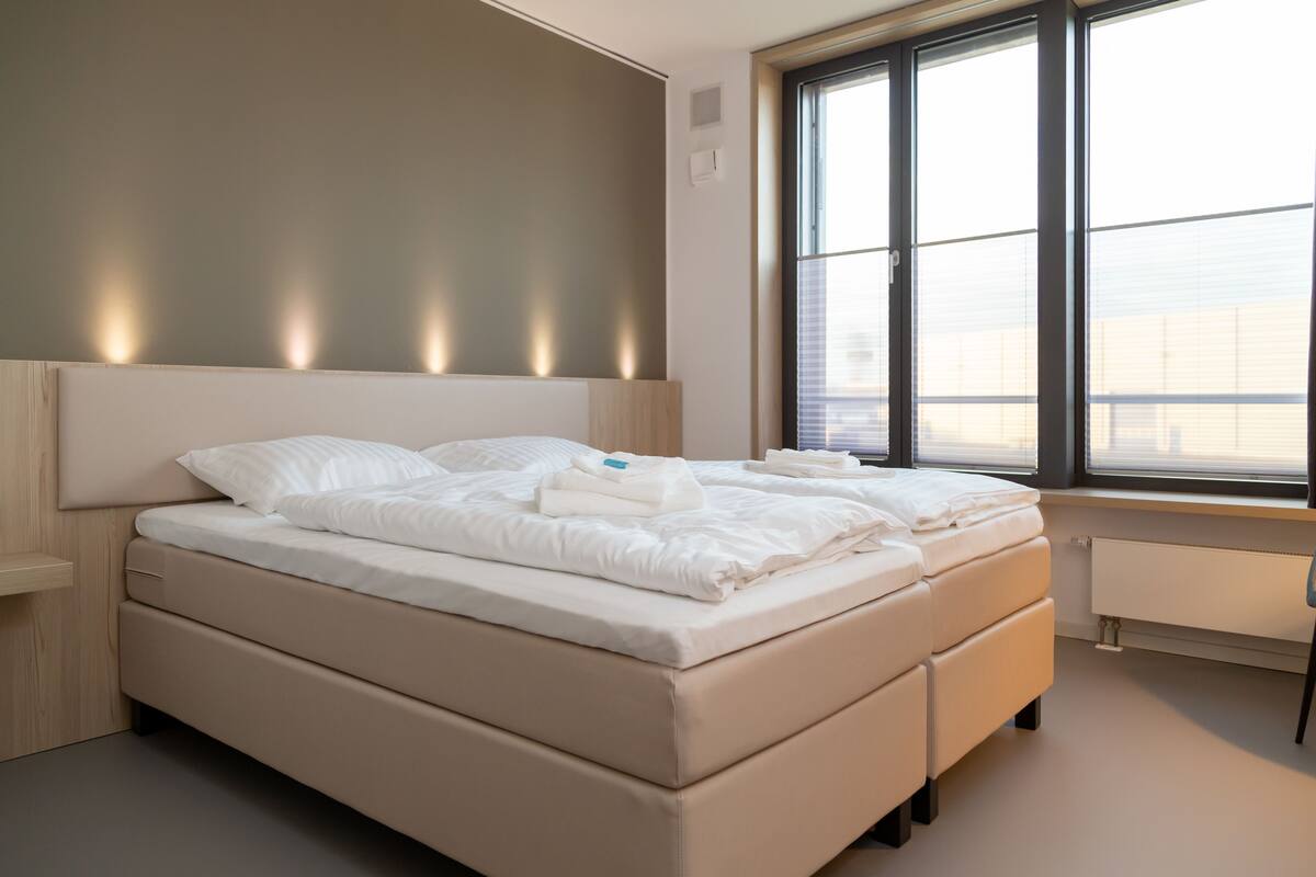 A modern bedroom with a large bed, built-in headboard, and a window with blinds.