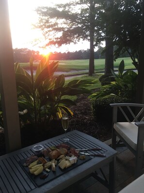 A patio with a table set for a meal, surrounded by greenery and a view of a golf course. - Sunset on 17 at TrueBlue (Pawleys Island)