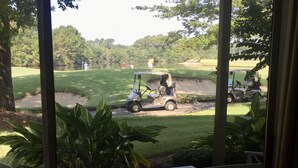 Ein überdachter Außenbereich mit zwei Holzbanken, Blick auf einen Golfplatz und ein Golfwagen in der Ferne.