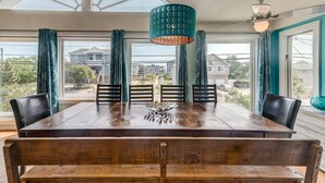 Ein Essbereich mit Holztisch und -stühlen, einer hängenden Leuchte und großen Fenstern mit Blick auf die Nachbarschaft.
