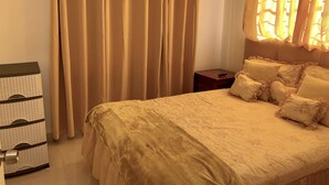 A bedroom with a bed, curtains, a bedside table, and a storage unit. - Higuey Center City, Candyland 2 bedroom  (Higüey)