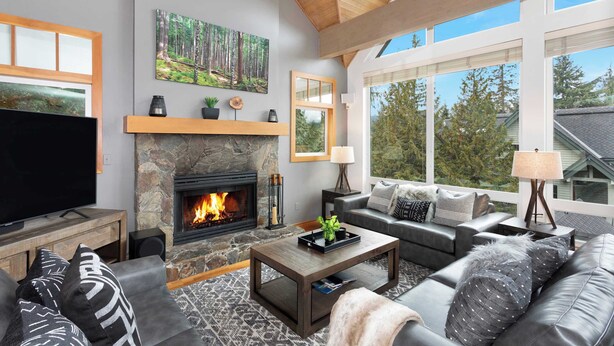 A modern living room with a stone fireplace, a large flat-screen TV, and a cozy seating area with a sofa and armchairs. - Alpine townhouse w/ hot tub & A/C (Whistler)