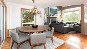 A modern living room with a round wooden dining table, grey upholstered chairs, a grey sofa, and a chandelier. - Alpine townhouse w/ hot tub & A/C (Whistler)