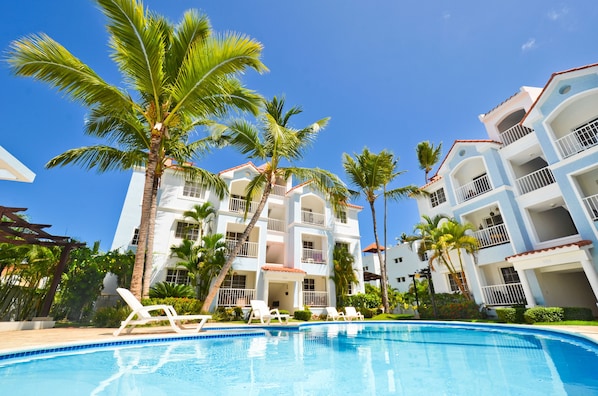 A hotel with a swimming pool, palm trees, and multiple balconies.