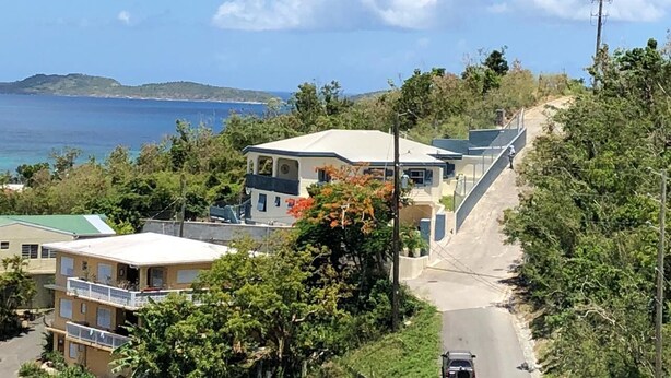 A coastal residential area with houses, a road, and a view of the sea. - Charming 1BR apt w/ balcony (St John)
