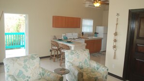 A kitchen with wooden cabinets, a dining area with two floral-patterned chairs, a small round table, and a ceiling fan. - Charming 1BR apt w/ balcony (St John)