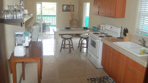 A kitchen with wooden cabinets, a stove, and a coffee maker. There are two stools and a table with a blender. - Charming 1BR apt w/ balcony (St John)