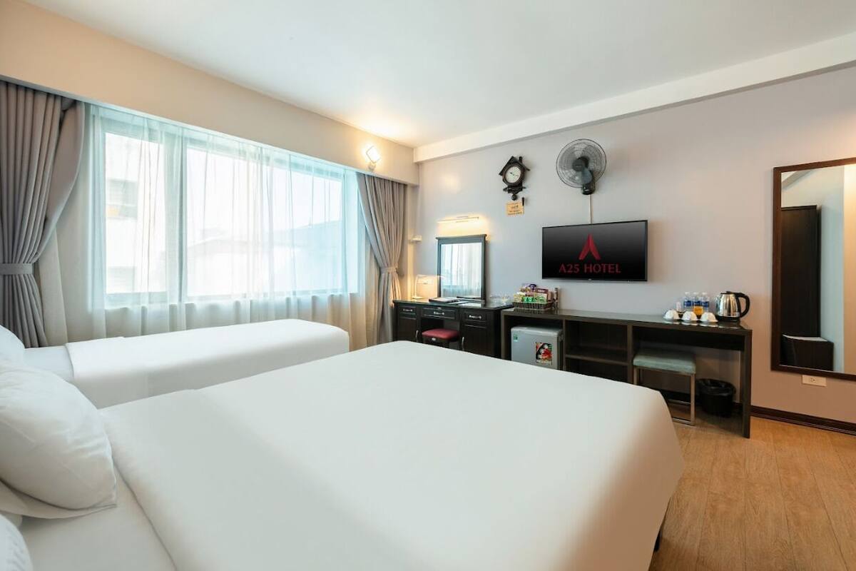 A hotel room with two beds, a desk, a TV, and a mirror.