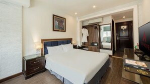 Une chambre d’hôtel avec un grand lit, une table de chevet avec une lampe, une armoire, un miroir et un téléviseur posé sur un meuble.