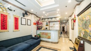 Un hall d’hôtel avec un comptoir d’accueil, un canapé bleu et un grand tableau floral accroché au mur.