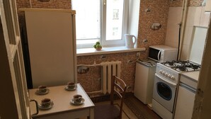 A compact kitchen with a stove, microwave, and a small refrigerator. There is a table with two cups of tea and a bowl of fruit on the windowsill. - Nostalgy House Moldova (Râşcani)
