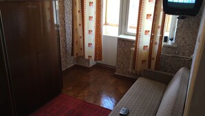 A room with a wooden wardrobe, patterned curtains, a red rug, a sofa, and a television displaying a digital interface. - Nostalgy House Moldova (Râşcani)