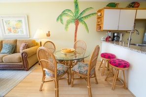 Un espace de vie compact avec une table ronde en verre entourée de chaises en osier, un canapé et un coin cuisine comprenant un évier et un plan de travail.