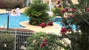 A pool area with a house in the background, surrounded by greenery and a fence. -  Welcome to SSI...near Pier, Village and Beach! (St Simons)