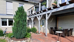 A modern house with a brick exterior, a covered patio with outdoor furniture, and a large coniferous tree. - Ferienwohnung Im Kleinen Feld (Waldeck)