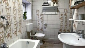 A bathroom with a bathtub, toilet, and sink, tiled with floral patterns. - Ferienwohnung Im Kleinen Feld (Waldeck)