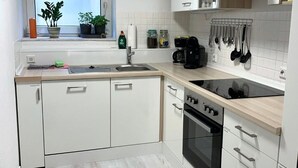 A modern kitchen with white cabinets, a black stove, and a window with plants. - Ferienwohnung Im Kleinen Feld (Waldeck)