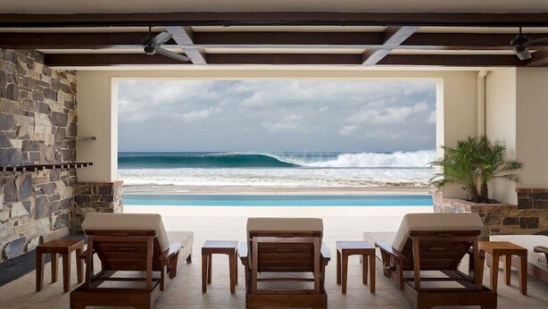 A poolside area with wooden lounge chairs and a view of the ocean. - Fort Walker (Beachfront House) (Hacienda Iguana)