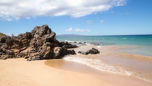 A beach with a rocky outcrop and calm waters.