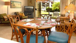 A dining area with a round table, blue cushioned chairs, and a television in the background.