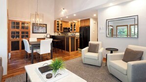 A modern living room with a dining area and kitchen, featuring wooden cabinets, a white sofa, and a coffee table. - Ski-in retreat w/ deck BBQ & mountain views (Whistler)