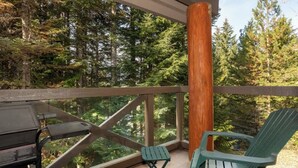 A balcony with a view of dense forest, a wooden post, a green Adirondack chair, and a grill. - Ski-in retreat w/ deck BBQ & mountain views (Whistler)