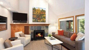 A modern living room with a fireplace, a flat-screen TV, and a large window. - Ski-in retreat w/ deck BBQ & mountain views (Whistler)