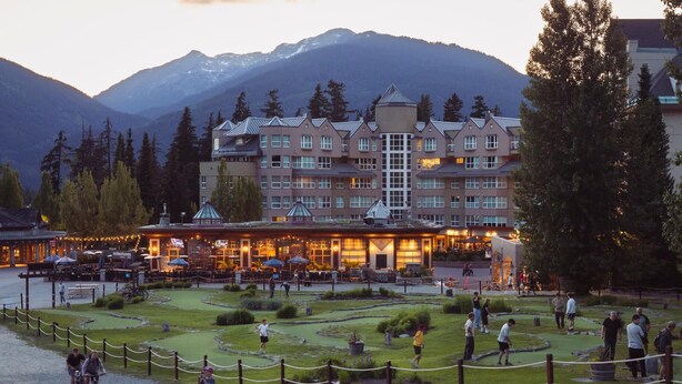 A hotel with a courtyard, outdoor seating, and a mountainous backdrop. - Ski-in retreat w/ deck BBQ & mountain views (Whistler)