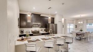 A modern kitchen with dark cabinets, stainless steel appliances, and a central island with bar stools. - 5BR Villa Bliss: Private Pool - Sleeps 14 - 412 (Davenport)